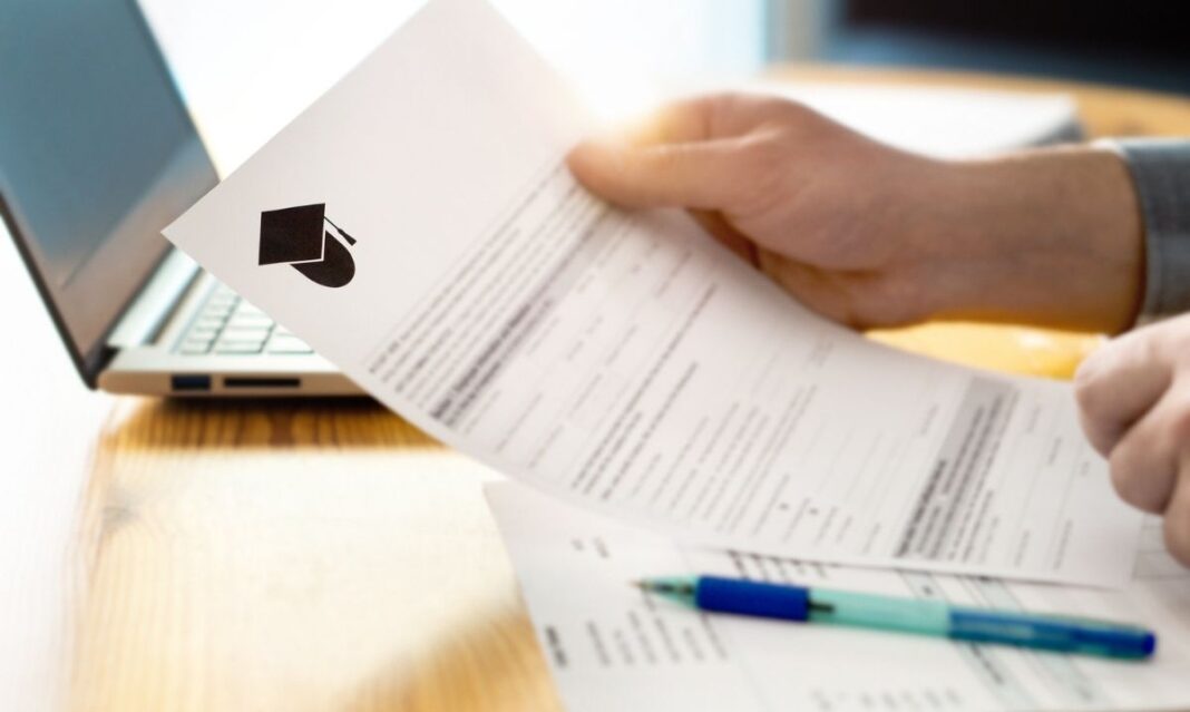 Person reviewing a student financial aid or college application form on a laptop with paperwork and pen