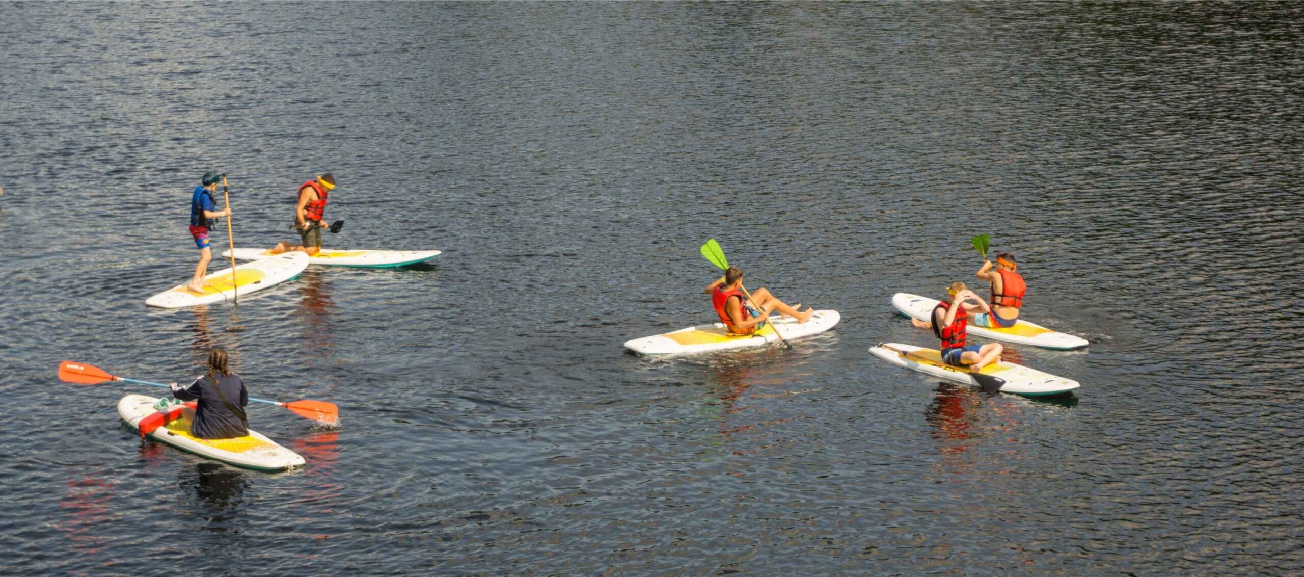 Campers paddleboard and kayak on the private lake at YMCA Camp Timbers overnight camp in Northern Michigan