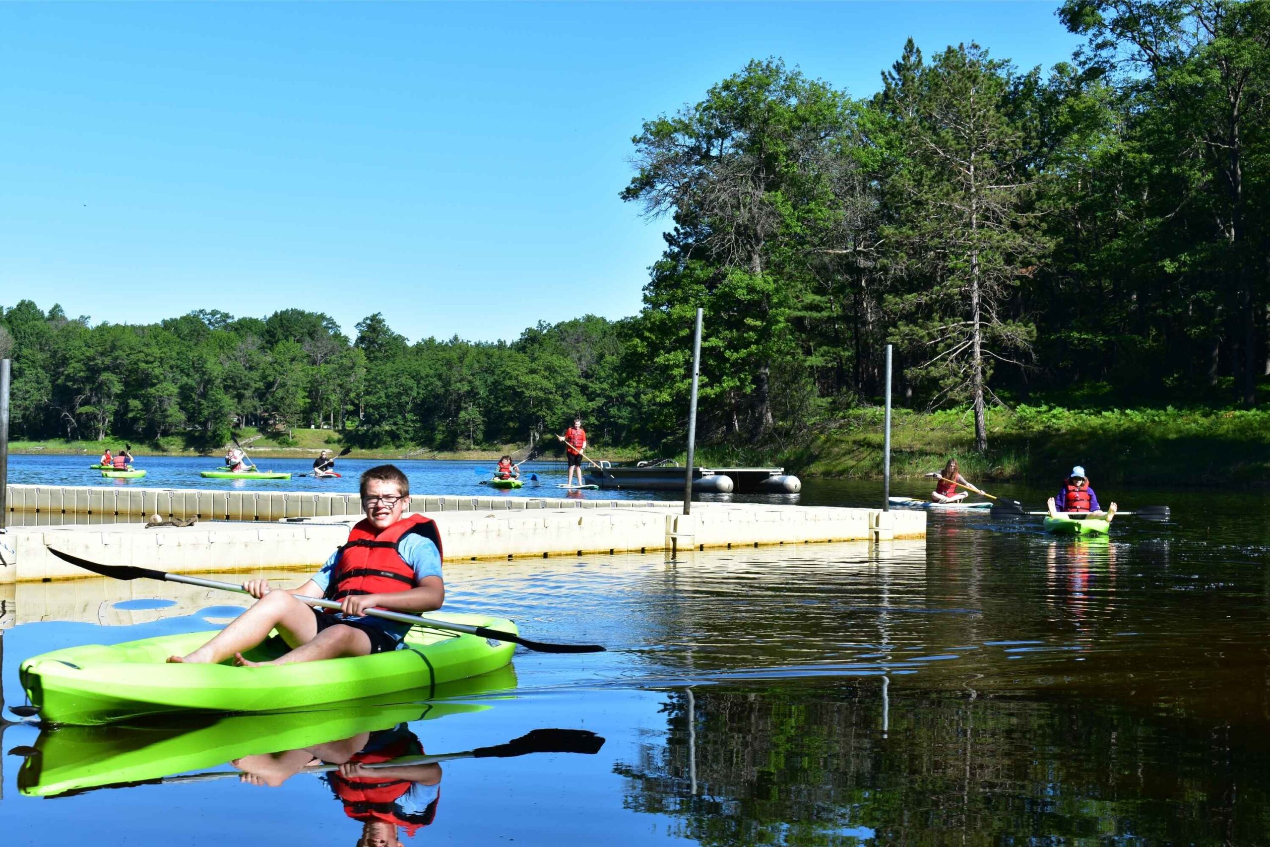 Campers kayak and paddleboard on the private lake at YMCA Camp Timbers overnight camp in West Branch, Michigan
